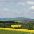 Panorama mit gelben Rapsfeldern, grünen Hügeln und dem Kaiser-Wilhelm-Denkmal am Horizont.