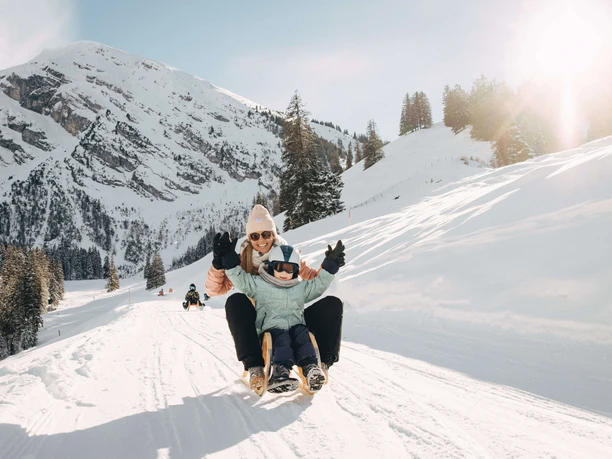 Les joies de la luge pour jeunes et moins jeunes La femme et l'enfant sont assis sur la luge et dévalent la petite route enneigée