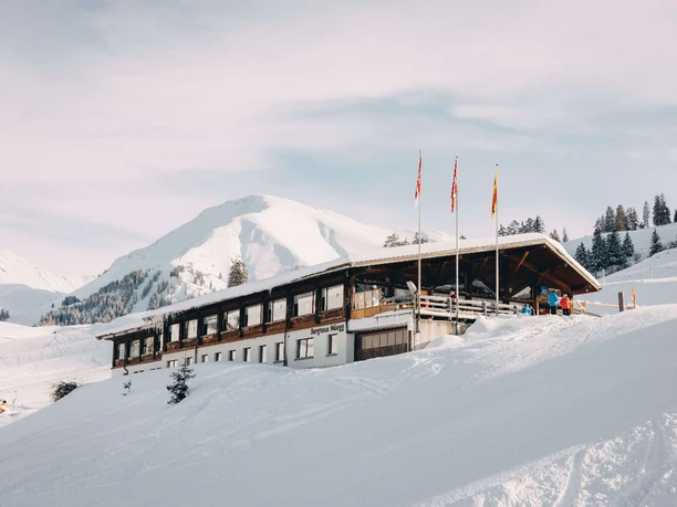 Berghotel Wiriehorn im Winter Verschneites Bergasthaus, davor stehen drei Fahnenmasten