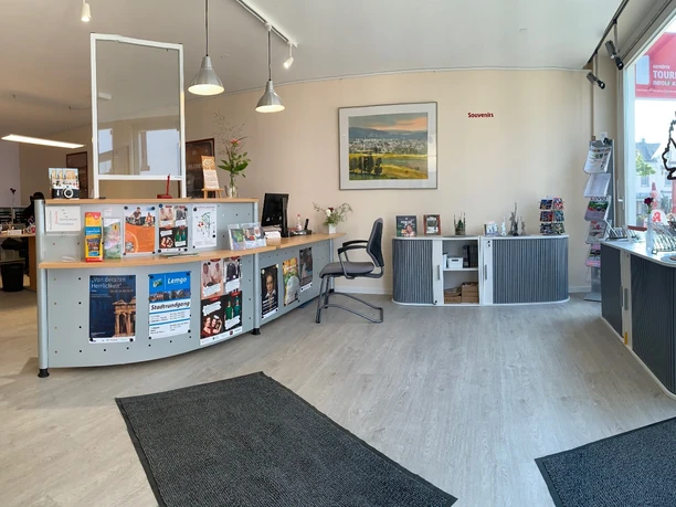 Tourist-Information & Souvenirs Ein moderner Infobereich mit Theke, verschiedenen Broschürenständern und Souvenir-Präsentation.