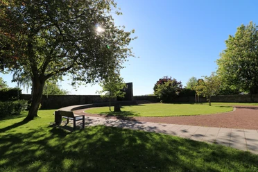Stadtpark im Sonnenlicht mit geschwungenen Wegen, Bänken und schattenspendenden Bäumen.