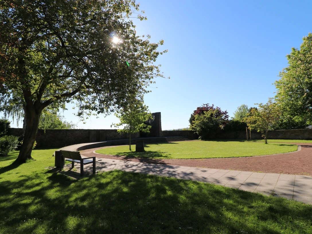 Stadtpark im Sonnenlicht mit geschwungenen Wegen, Bänken und schattenspendenden Bäumen.