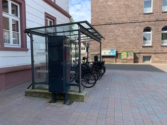 Fahrradständer mit Überdachung an einem gepflasterten Platz zwischen historischen Gebäuden.