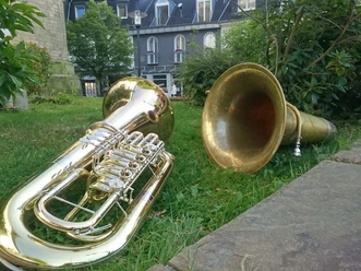 Zwei goldene Tuben liegen im grünen Gras vor einem Gebäude mit schiefergrauer Fassade.