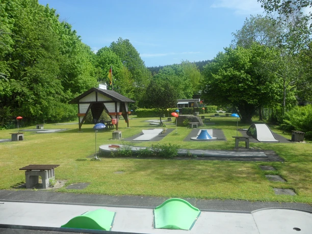 Minigolfplatz in Reichshof-Eckenhagen Minigolfplatz mit gepflegten Grünflächen, bunten Hindernissen, umgeben von Bäumen an einem sonnigen Tag.