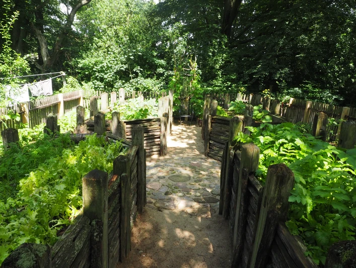 OLYMPUS DIGITAL CAMERA Steinerne Beeteinfassungen umrahmen eine Mischung aus grüner Vegetation und hellem Steinpfad.