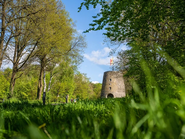 Kumsttonne Oerlinghausen "Frühsommeransichten" Alte Windmühle aus Stein in grünem Park mit blauem Himmel und vereinzelten Wolken im Hintergrund.