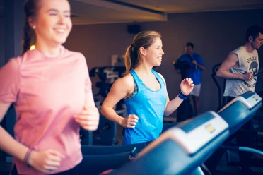 Fitness Zwei junge Frauen und ein Mann trainieren fröhlich auf Laufbändern in einem modernen Fitnessstudio.
