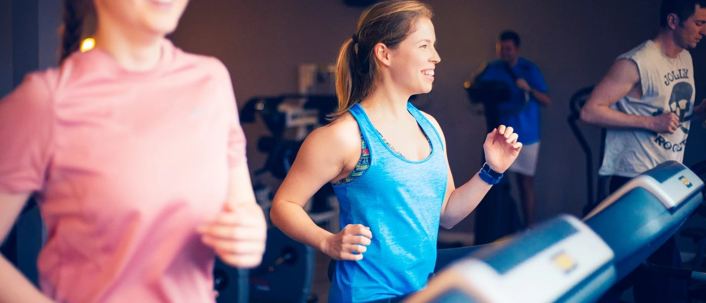 Fitness Zwei junge Frauen und ein Mann trainieren fröhlich auf Laufbändern in einem modernen Fitnessstudio.