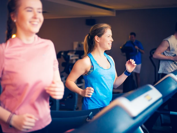 Fitness Two young women and a man are happily exercising on treadmills in a modern fitness studio.