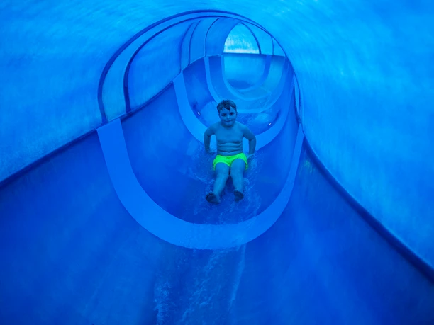 Erlebnisbad A little boy slides down a blue water slide.