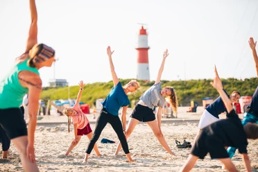 A group of colorfully dressed people doing yoga on the beach.