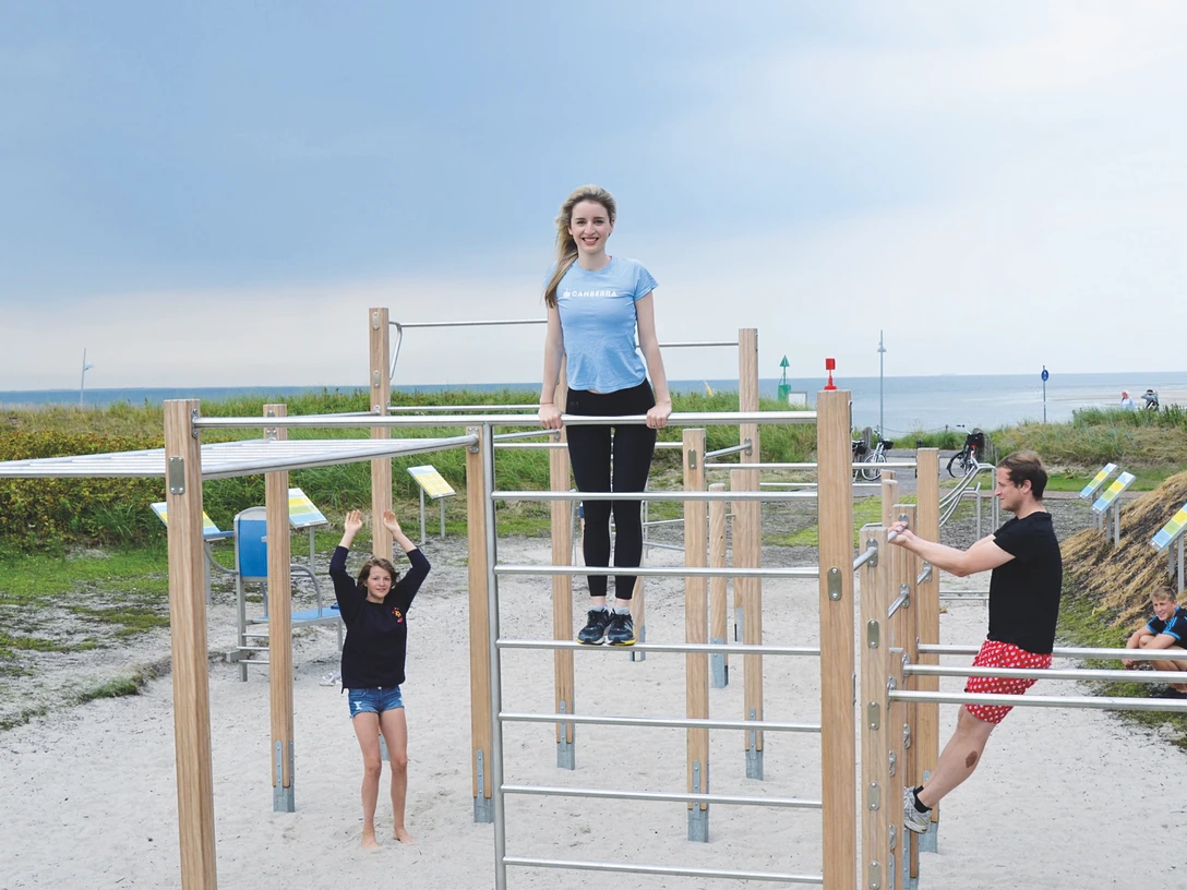 Mehrere sportlich gekleidete Personen machen Sport auf dem Outdoor-Bewegungsparcours vor der Nordsee. Several athletically dressed people are exercising on the outdoor exercise trail in front of the North Sea.