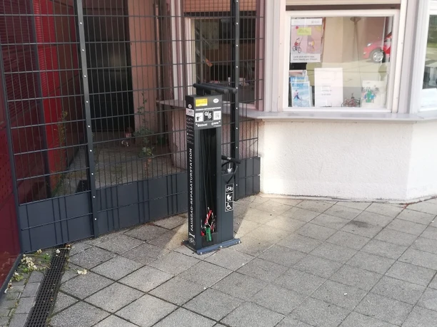 Servicesäule an einer Fahrradstation mit Werkzeugen zur Fahrradreparatur, auf einem gepflasterten Boden.