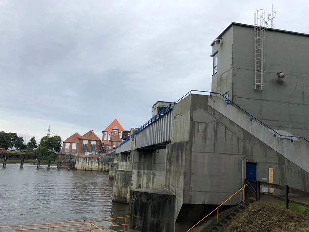 Wehr in Dörverden mit grauen Betonwänden, Treppe, Geländer, und dahinterliegendem Flussabschnitt.
