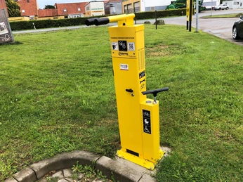 Gelbe Luftpumpenstation für Fahrräder auf grünem Rasen in einer städtischen Umgebung.