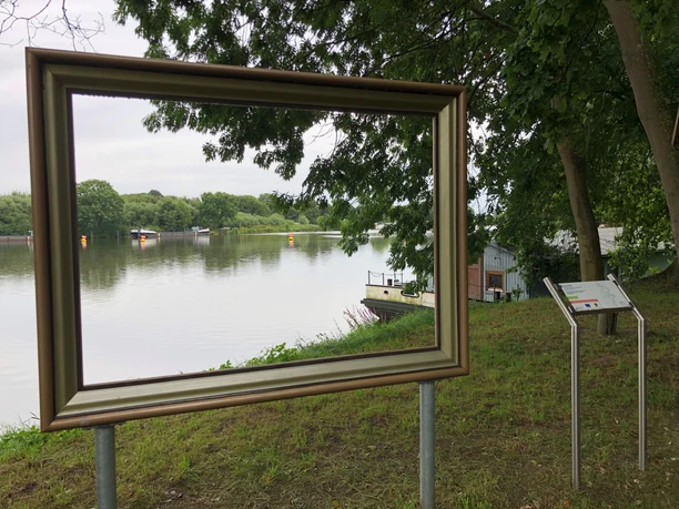 Ein großer Bilderrahmen an der Weser lenkt den Blick auf das ruhige Flussufer und die Umgebung.
