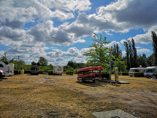 Reisemobilstellplatz_Rhauderfehn_04 Sonniger Stellplatz mit Wohnmobilen, einer Versorgungssäule und roten Kanus auf einem Anhänger.