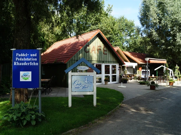 Reisemobilstellplatz_Rhauderfehn_05 Grünes Holzhaus mit Schildern für das Café am Siel und die Paddel- und Pedalstation.