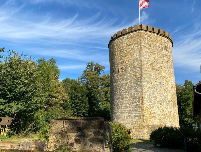 Burg Ravensberg in Borgholzhausen Rundturm der Burg Ravensberg in Borgholzhausen, umgeben von Bäumen unter blauem Himmel mit Wolken.