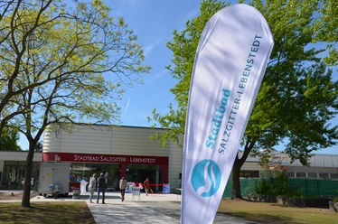 Eingang zum Stadtbad Salzgitter-Lebenstedt Eingangsbereich des Stadtbads Salzgitter-Lebenstedt mit Besuchern und Fahne vor dem modernen Gebäude.