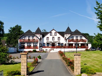 Außenansicht Hotel Freihof Hotel Freihof mit Fachwerkfassade, Türmen und gepflegter Gartenanlage unter blauem Himmel.