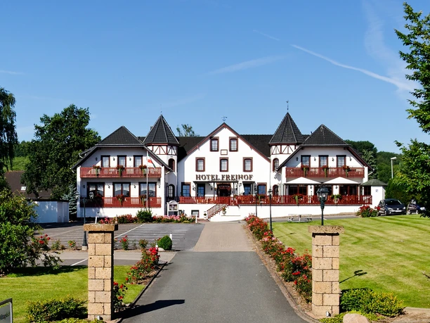 Außenansicht Hotel Freihof Hotel Freihof mit Fachwerkfassade, Türmen und gepflegter Gartenanlage unter blauem Himmel.
