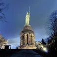 Hermannsdenkmal Beleuchtetes Hermannsdenkmal bei Nacht, umgeben von Bäumen, unter einem klaren Nachthimmel.