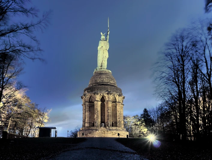 Hermannsdenkmal Beleuchtetes Hermannsdenkmal bei Nacht, umgeben von Bäumen, unter einem klaren Nachthimmel.