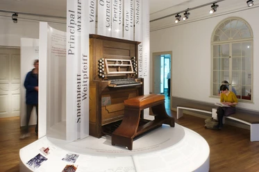 (c) Bach-Museum Leipzig, Jens Volz_305.JPG Holzorgel im Bach-Museum Leipzig, umgeben von Informationstafeln und Besuchern.