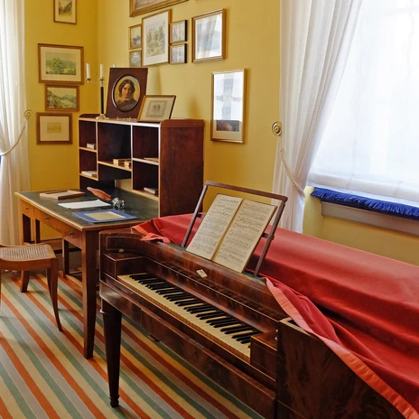 A room with a historic writing desk and piano in warm colors.