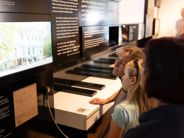 Three people look with interest at interactive screens in a modern exhibition cabinet.
