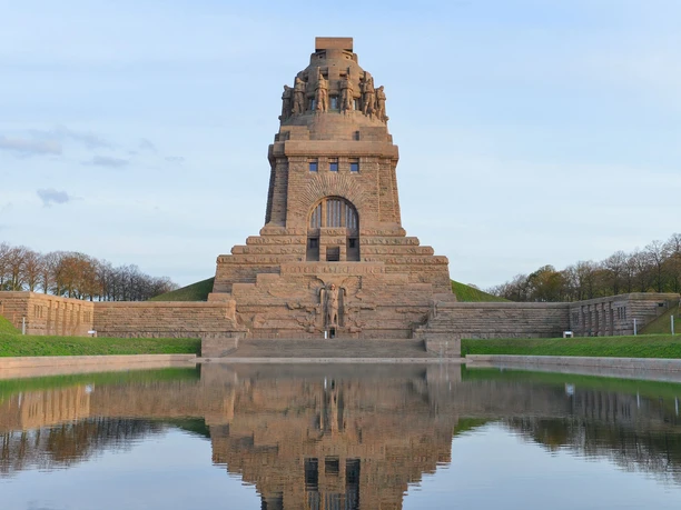 Monument to the Battle of the Nations in Leipzig, reflected in the water, surrounded by a green park.