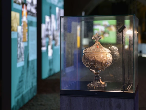 Glass display case with decorated lidded goblet, illuminated in a modern showroom.