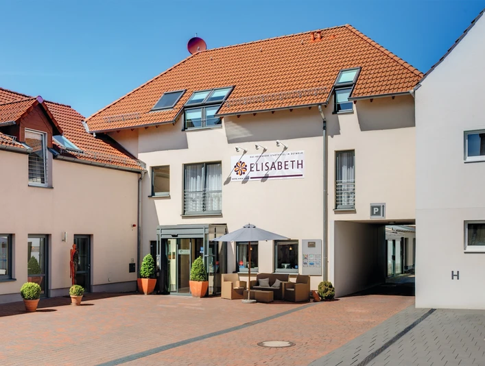 Hotel Elisabeth mit roten Ziegeldächern, begrünten Eingangspflanzen und Sitzbereich im Vordergrund.