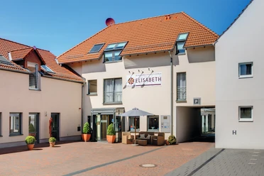 Außenansicht Hotel Elisabeth Hotel Elisabeth mit roten Ziegeldächern, begrünten Eingangspflanzen und Sitzbereich im Vordergrund.