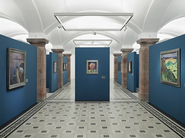 02_KuC_DA Schmidt-Rottluff 01_Foto PUNCTUM Bertram Kober.jpg Museumsausstellung mit Gemälden von Schmidt-Rottluff in einem Raum mit blauen Wänden und Säulen.