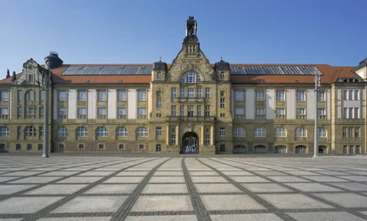 01_KuC_Kunstsammlungen Chemnitz_außen_Foto_PUNCTUM_Bertram Kober_verkleinert.jpg Kulturhaus mit beeindruckender Architektur und großem gepflastertem Vorplatz unter blauem Himmel.