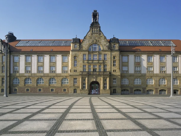 01_KuC_Kunstsammlungen Chemnitz_außen_Foto_PUNCTUM_Bertram Kober_verkleinert.jpg Kulturhaus mit beeindruckender Architektur und großem gepflastertem Vorplatz unter blauem Himmel.