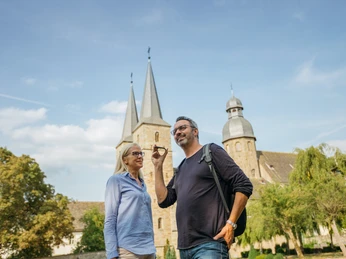 Marienmuenster-Abteikirche-Teutoburger-Wald-Tourismus-M-Schoberer (2).jpg Zwei Personen vor der imposanten Abteikirche im Teutoburger Wald, klarer Himmel im Hintergrund.