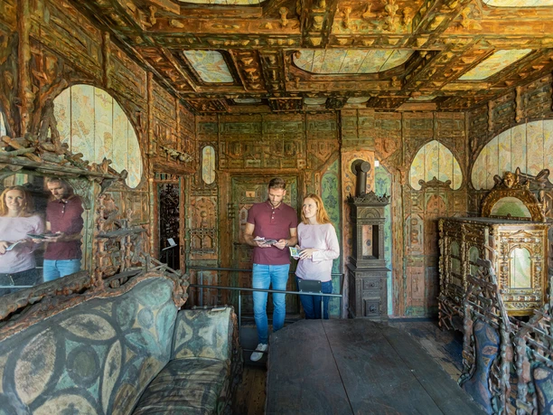 Lemgo-Junkerhaus-Teutoburger-Wald-Tourismus-M-Schoberer (9).jpg Holzvertäfelter Raum im Junkerhaus mit detaillierten Schnitzereien; zwei Personen betrachten Broschüren.