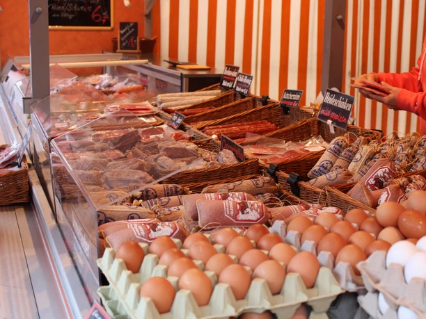 Wochenmarkt in Rastede Ein Marktstand mit frischen Eiern, verpackten Würsten und Schinken. Ein Verkäufer bedient Kunden.