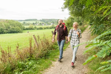 Nümbrecht Zwei Personen wandern auf einem ländlichen Pfad, umgeben von grüner Landschaft und Bäumen.