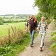 Nümbrecht Zwei Personen wandern auf einem ländlichen Pfad, umgeben von grüner Landschaft und Bäumen.
