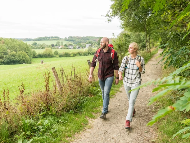 Nümbrecht Zwei Personen wandern auf einem ländlichen Pfad, umgeben von grüner Landschaft und Bäumen.