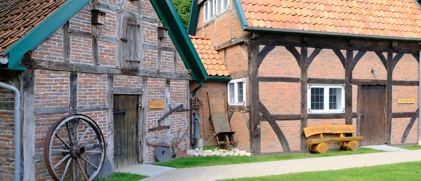 Heimatmuseum Wiefelstede Zwei Fachwerkgebäude mit roten Ziegeldächern und einem großen hölzernen Wagenrad.