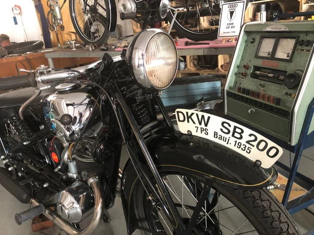 Eine DKW SB 200 von 1935, dunkel in Farbe, steht vor einer alten Werkstattanzeige.