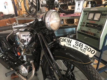 Motorradmuseum Eystrup Eine DKW SB 200 von 1935, dunkel in Farbe, steht vor einer alten Werkstattanzeige.