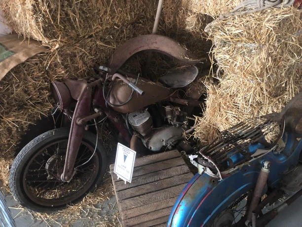 Ein altes Motorrad steht zwischen Strohballen in einem rustikalen Raum des Motorradmuseums Eystrup.