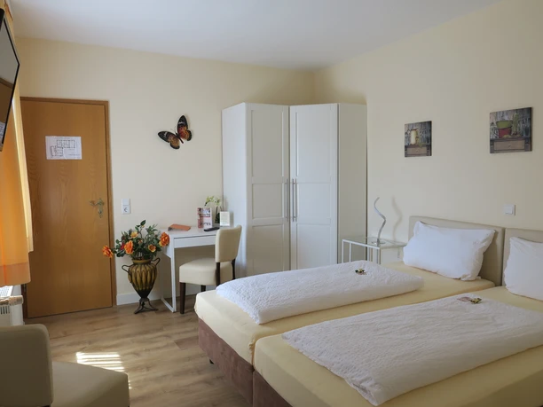 Landhotel Bergischer Hof Marialinden Doppelzimmer mit zwei Einzelbetten, heller Einrichtung, Schreibtisch, Fernseher und Dekoration.